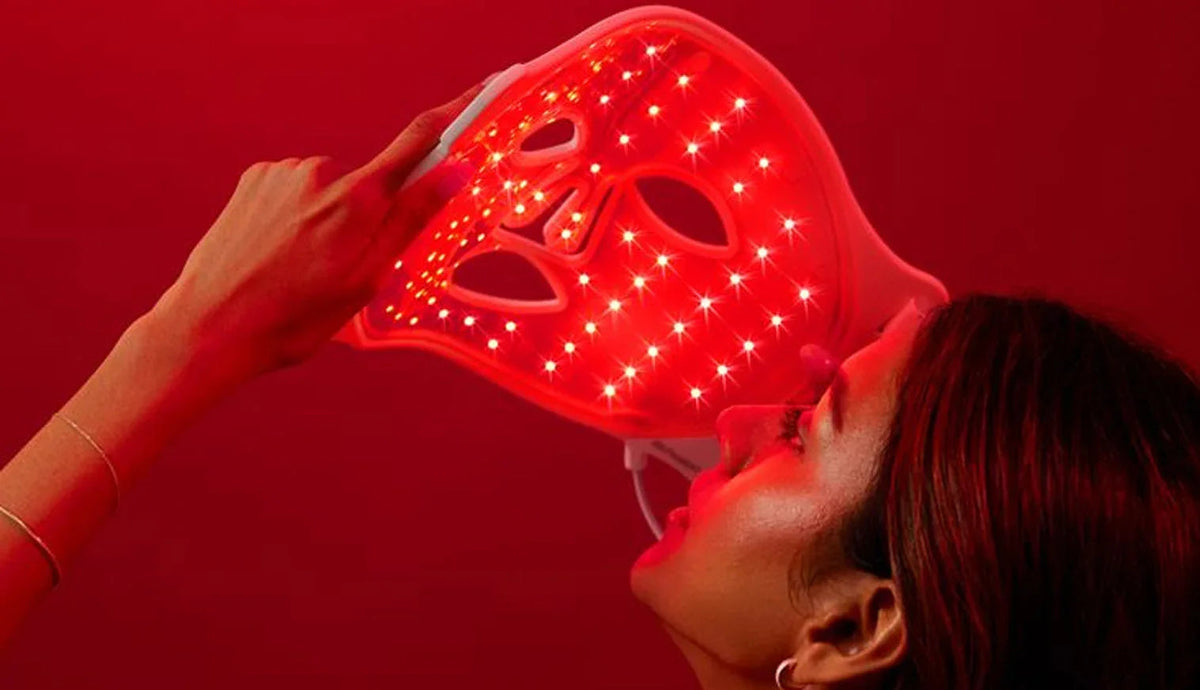 Woman using red LED light therapy mask for acne and anti-aging skincare at home